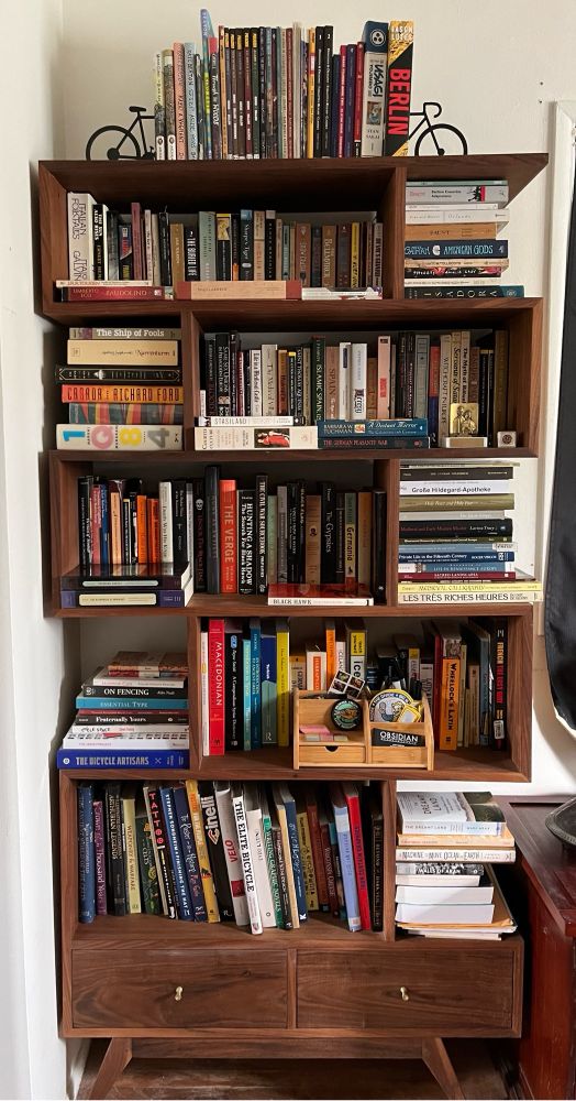 A bookshelf with a bunch of books, mostly history books with some novels and bike photography 