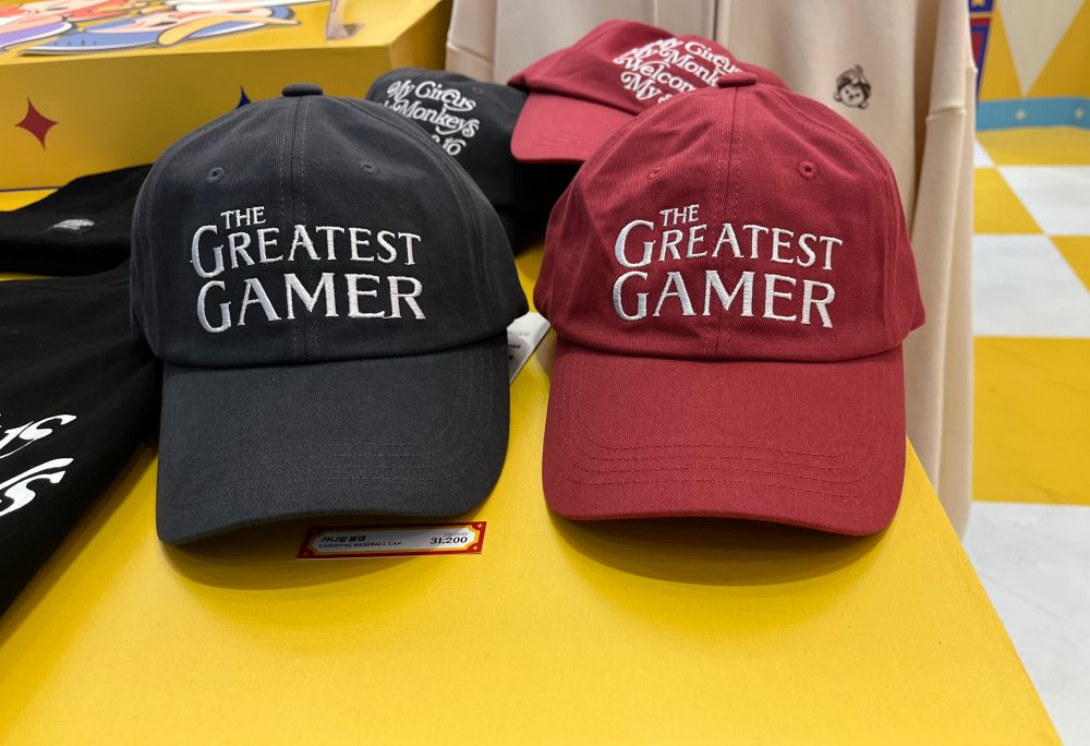 Two baseball hats that say The Greatest Gamer (left, grey, right, red)