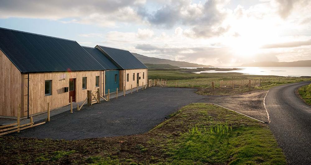 Photograph shows two timber passive houses side by side, overlooking the bay at Ulva Ferry in Scotland