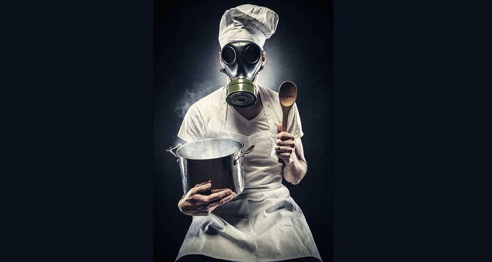 Picture shows a chef holding a cooking pot, while wearing a gas mask, to highlight the health risks from indoor air quality in a kitchen