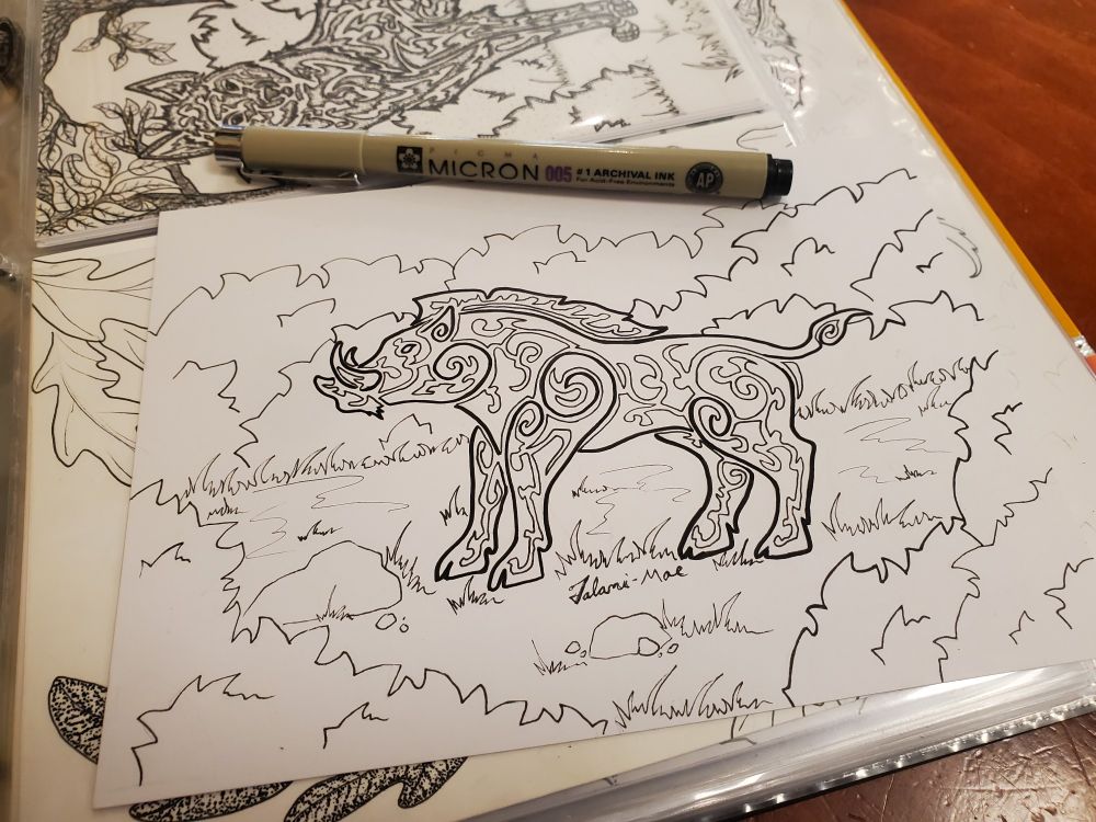 Photo taken of a traditionallt drawn stylized boar standing in the grass, bushes in the forground and background

It stands facing left, penned in ink, mid process on top of my art binder