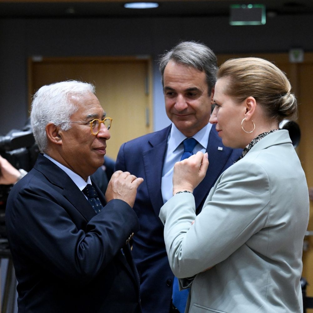 Three people looking at each other. On the right a man in a blue suit (European Council president). In front of him a blond women in a beige suit. Behind a man in a blue suit looking in the direction of the European council president. 