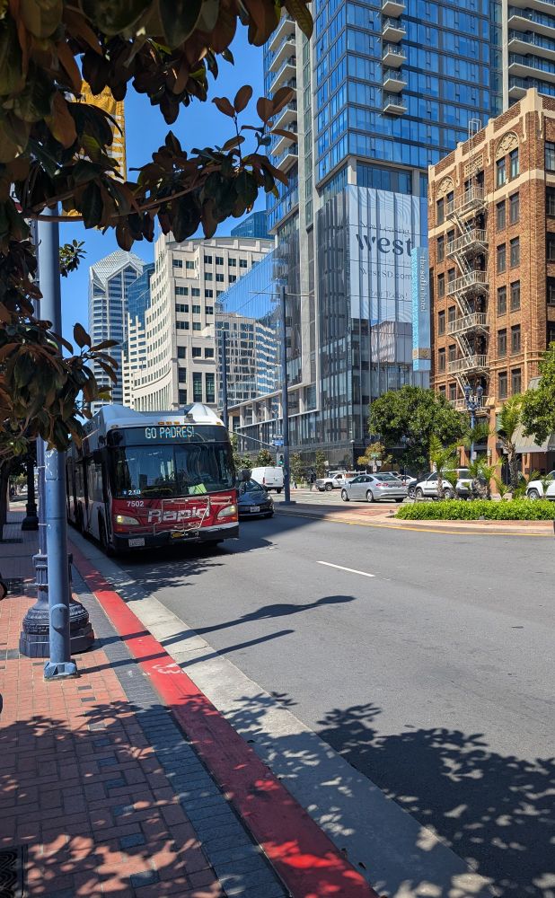 Street called Broadway in Downtown San Diego with a Rapid bus in foreground and a mix of historic brick building and modern glass and concrete high rise in the background.