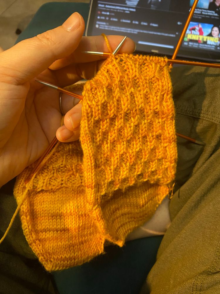The Honeycomb Socks by Emily Bolduan are being worked on double pointed needles in a bright mustard yellow- it's KnitPicks Stroll Tonals in Poppy Fields. 
The hand holding them isn't actually suffering from acute jaundice, it's just being in the presence of yellow yarn. #knitting