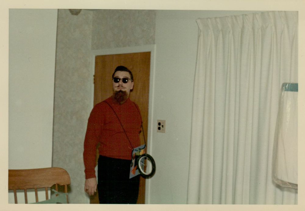 A young man dressed as a beatnik stands in a mid-century modern living room.