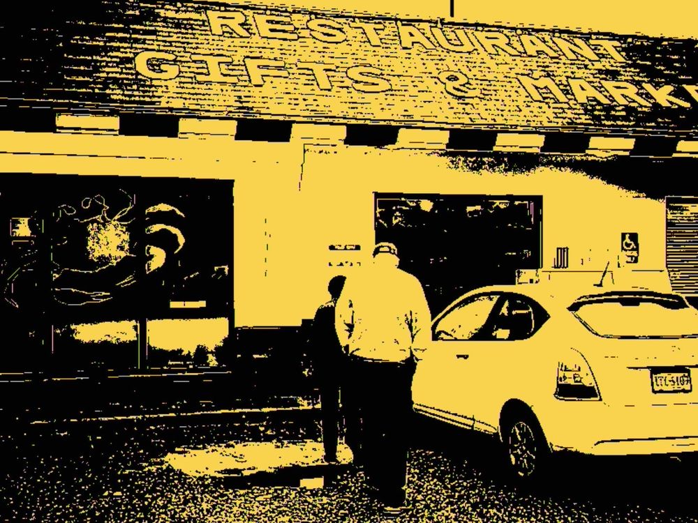 A couple walks towards a building with a sign on it that reads Restaurant Gifts & Market. The restaurant is The Great Machipongo Clam Shack, housed in a converted McDonalds 