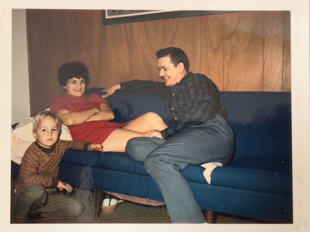 1960s Polaroid of a married couple smiling on a solid blue couch and a young blonde boy looking at the camera