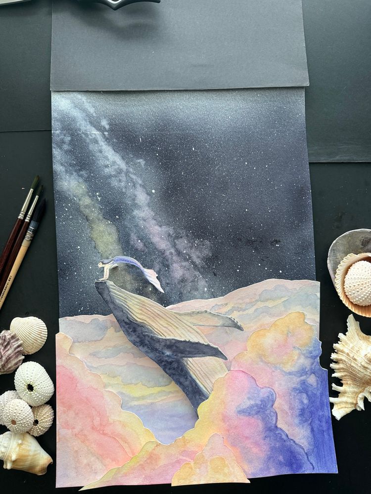 Multilayered, handcut, 3 dimensional watercolor painting featuring a humpback whale and tiny mermaid companion breaching through cotton candy-colored clouds of vibrant pinks, sunset orangey yellows and sleepy violets. Beyond the clouds, the Milky Way ribbons it’s way across the sky.