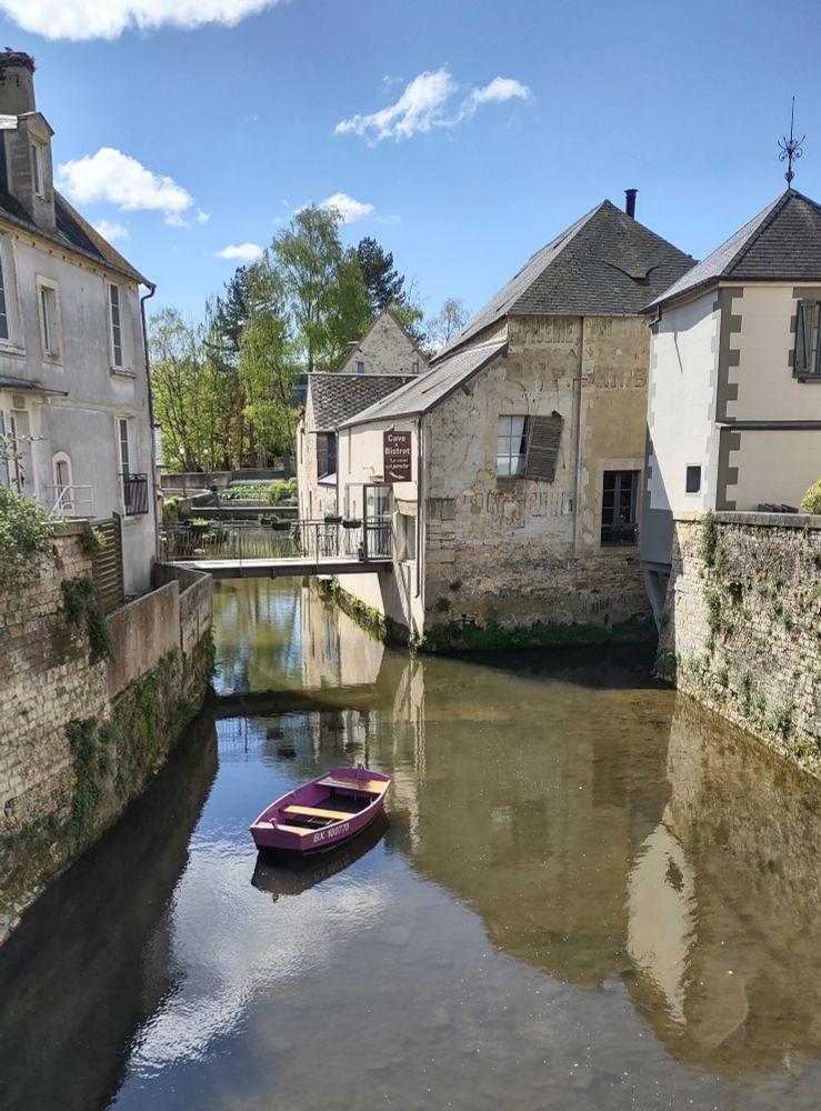 Stone building line a quiet waterway.  A small purple boat drifts in the middle 