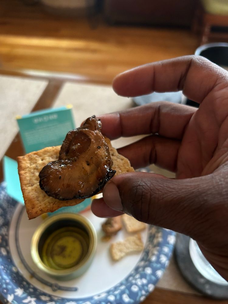 a ping pong ball sized smoked oyster on a cracker being held above a paper plate