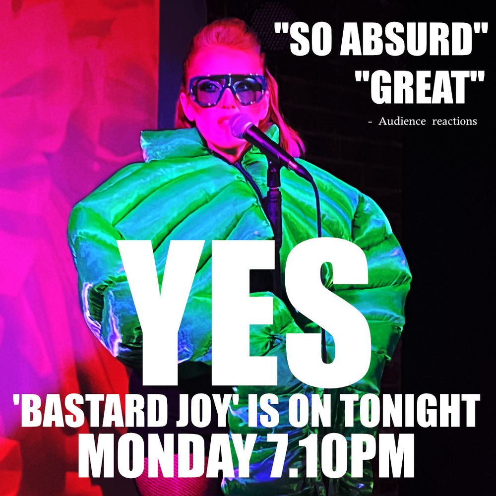 Artsy looking redheaded woman in green sunglasses and a ridiculous over-sized puffer jacket standing at a microphone in hot pink light. 