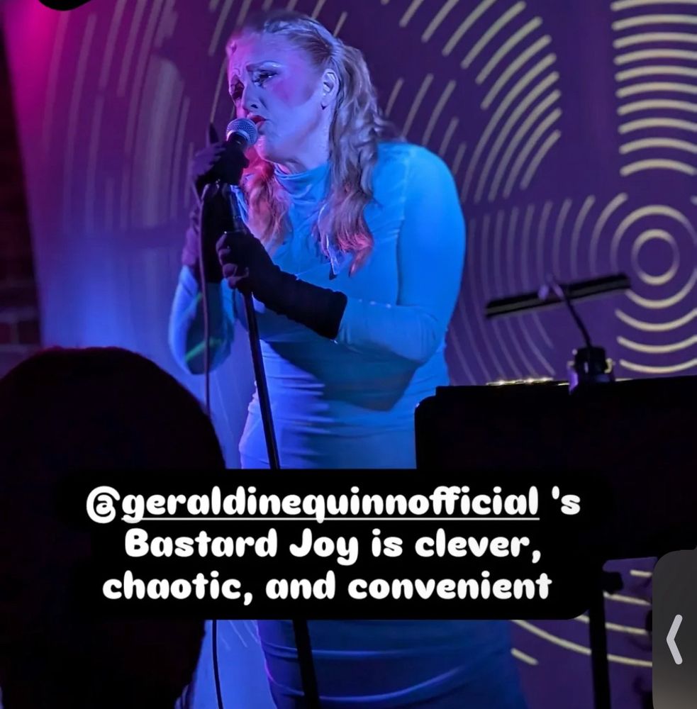 A middle-aged redheaded woman singing onstage bathed in blue light, wearing a blue wiggle dress with the quote “Geraldine Quinn’s Bastard Joy is clever, chaotic and convenjent” superimposed over the image.