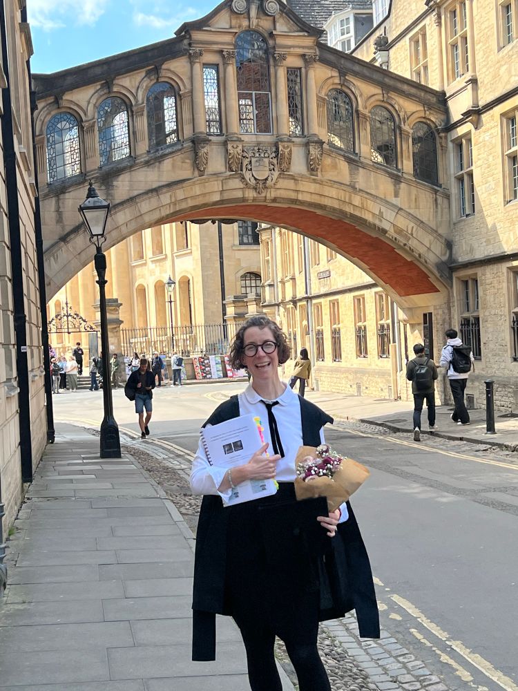 Oxford PhD student wearing black and white exam garb and a huge grin after successful defence!