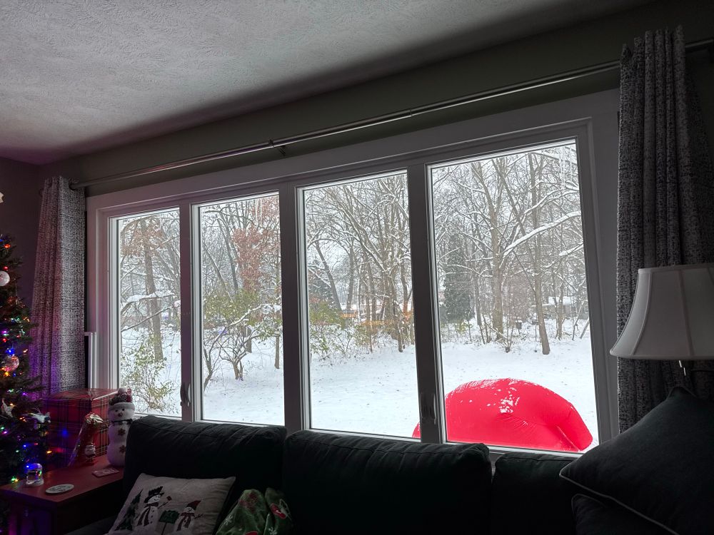 Left has the sliver of a lighted Christmas tree, with a set of four windows center and a lamp on the right. A red “dome” of an inflatable seen through the windows. 