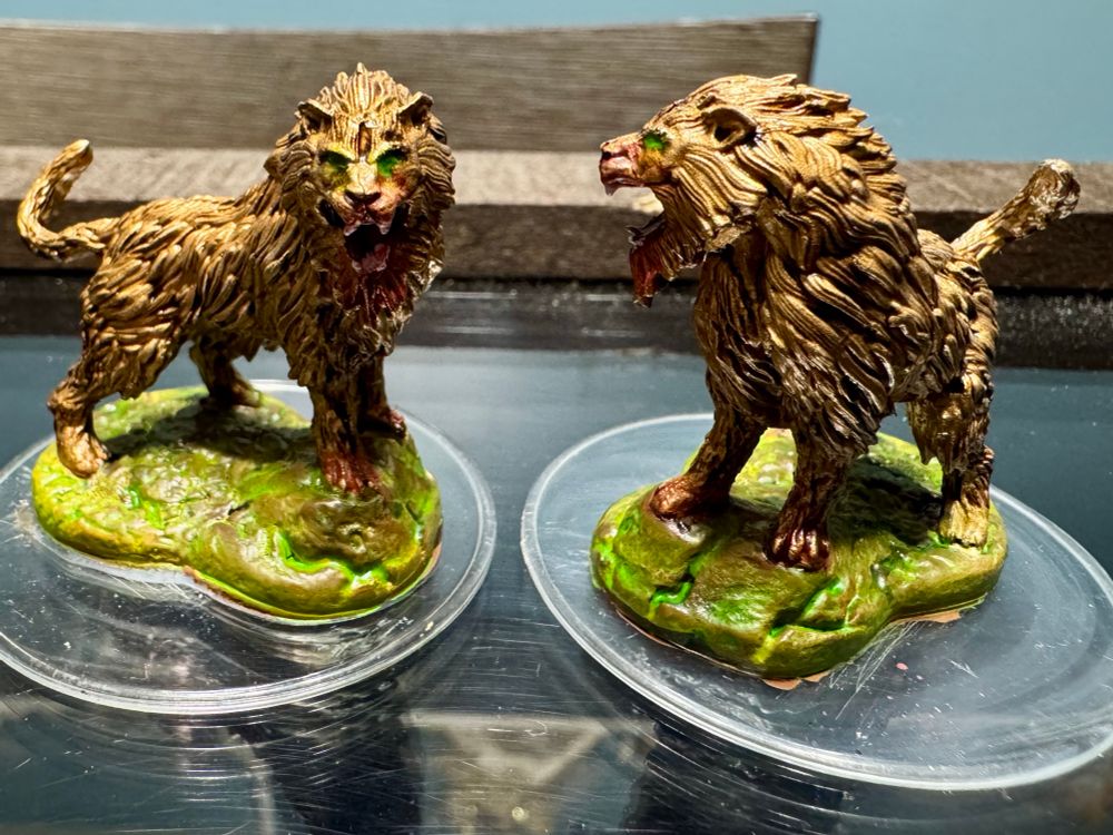 Mini figures on clear bases with painted pedestals- brown and green pedestals, gold base for fur coats with earthen colored washes, white teeth with red washes on mouths and front paws, green glowing eyes for effect. These are D&D Crag Cats that I’ll be using as Golden Lions. 