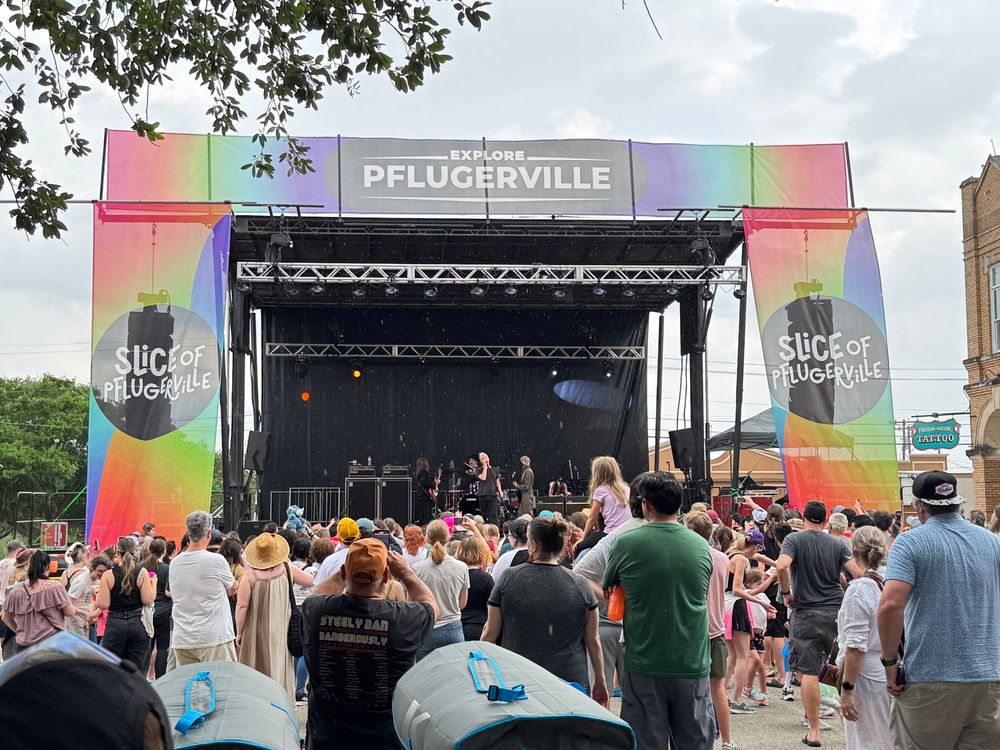 A large outdoor stage with a rainbow-colored proscenium and middle-aged band the Spin Doctors playing
