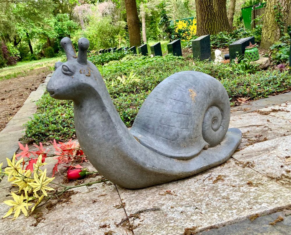 Graue Schnecke aus Stein, im Hintergrund sind Grabsteine