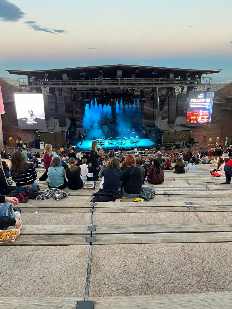 Red rocks amphitheater around dusk. People are seated on the cement stands and the stage lighting is blue
