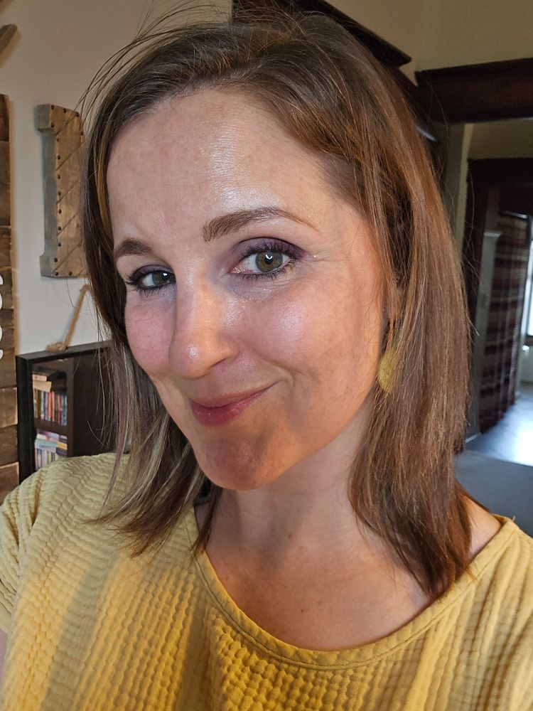 Brown haired woman wearing a yellow top smiling at the camera.  