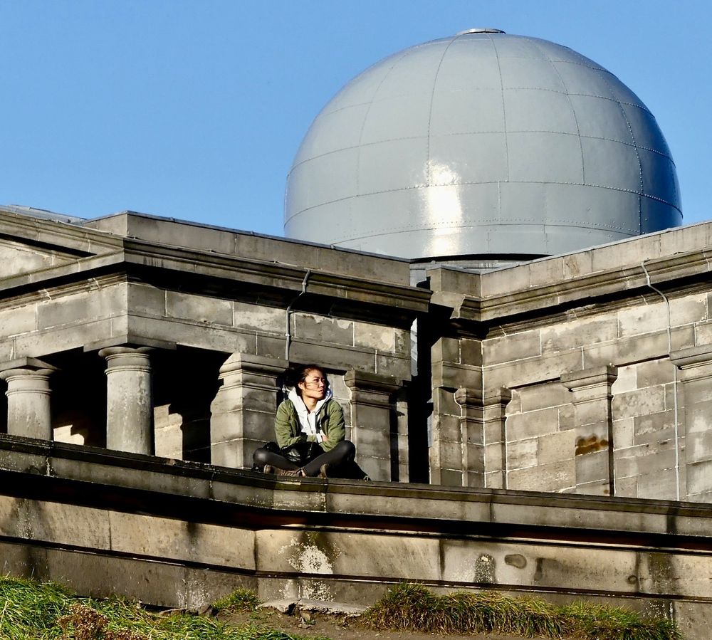 A pensive young woman sits alone, staring into the distance. The City Observatory in the background.