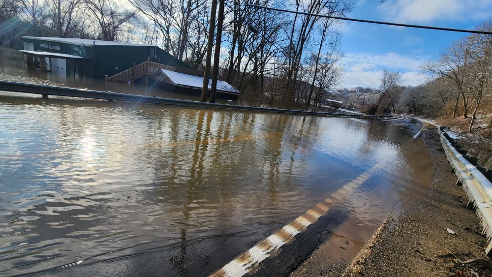 Photo showing the road covered with water, especially along the left/east side. Garrett's Golf Garage on the left is flooded out as well.
