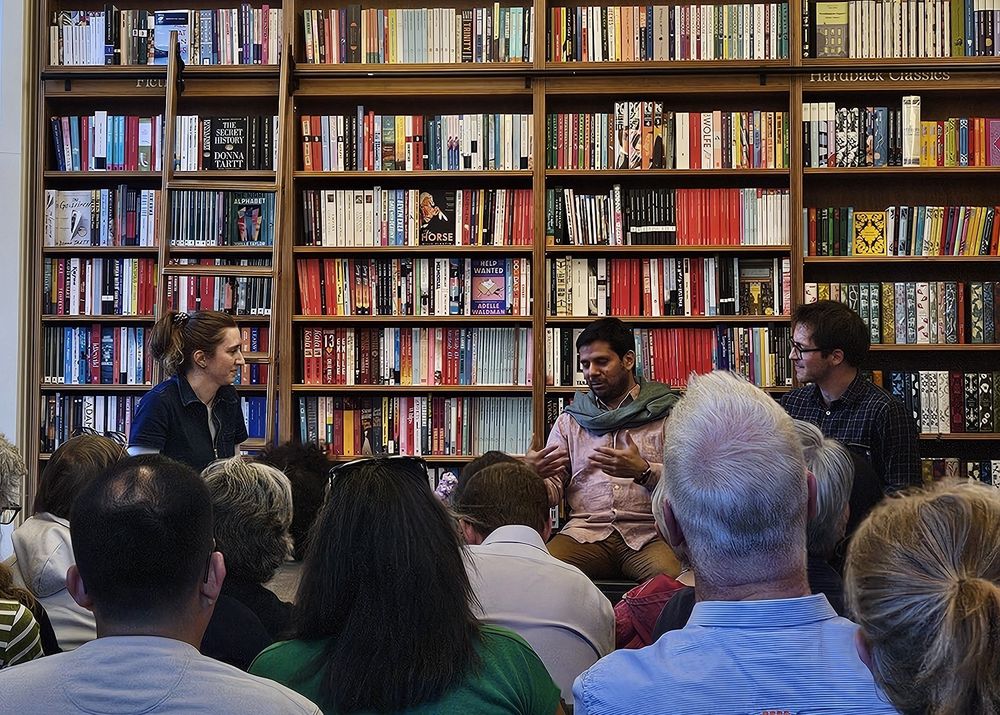 Renato talking to translator Dylan and bookseller Rachel in front of huge bookshelves 