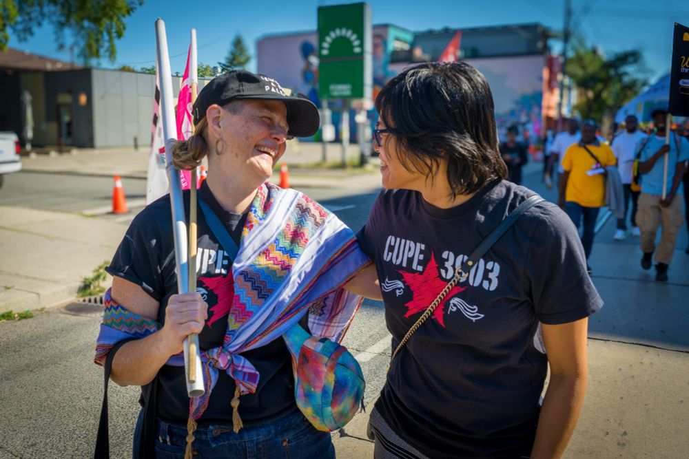 Two CUPE 3903 members, one with flags, smiling and conversing.
