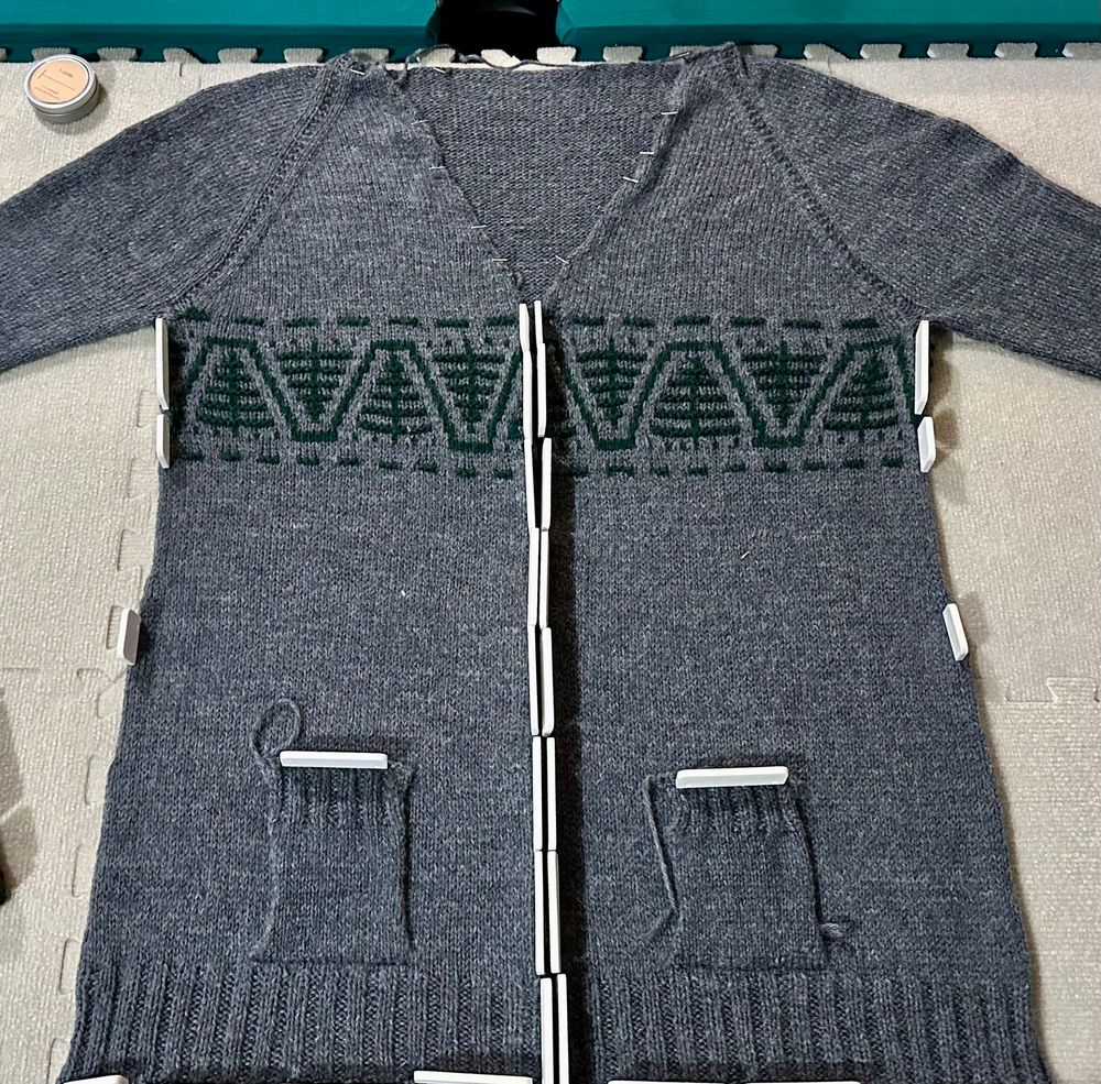 Photo of a nearly complete handknit gray cardigan, with a green tree accent.