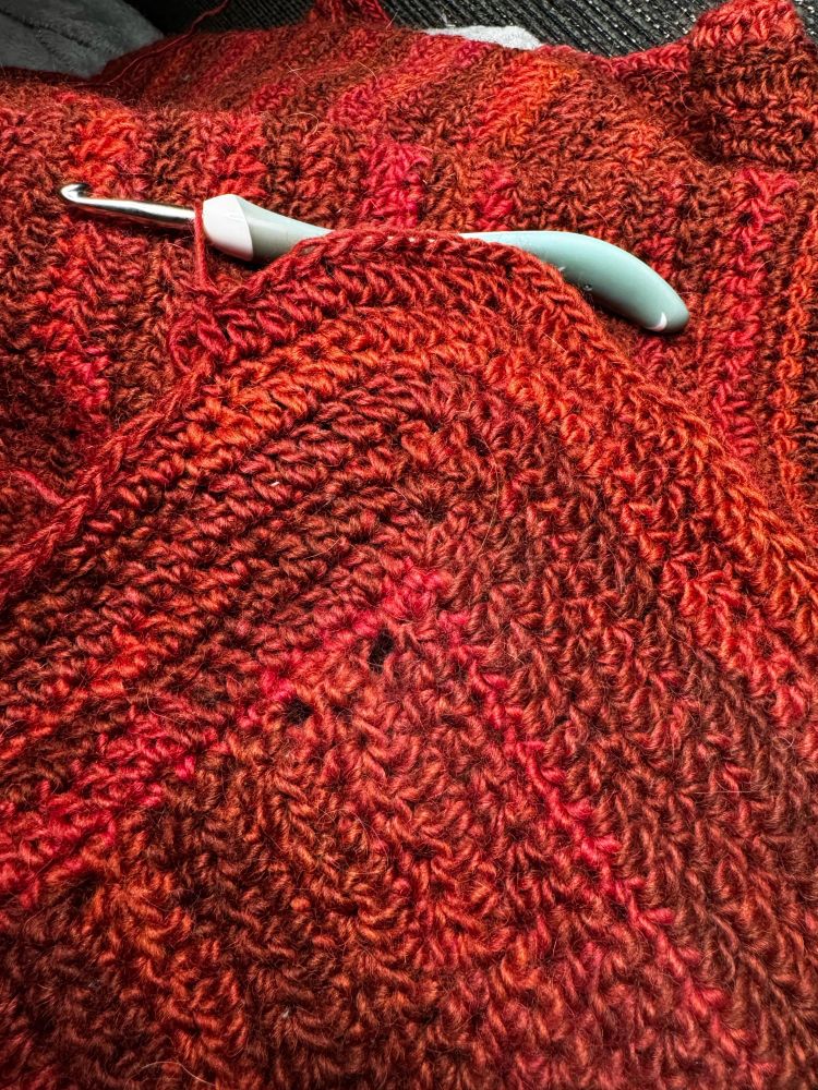 The blanket in progress - a mottled red chunky yarn crocheted in a wave-like pattern.