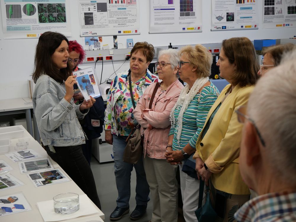En un laboratorio, una científica muestra un ejemplo de aplicación de su investigación. Las visitantes, alumnas de la Univaersidad de Mayores, observan la explicación.
