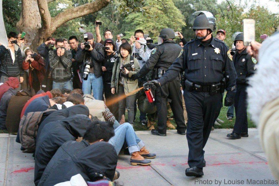 A Police Officer spaying Military grade pepper spray at students sitting in peaceful protest. 