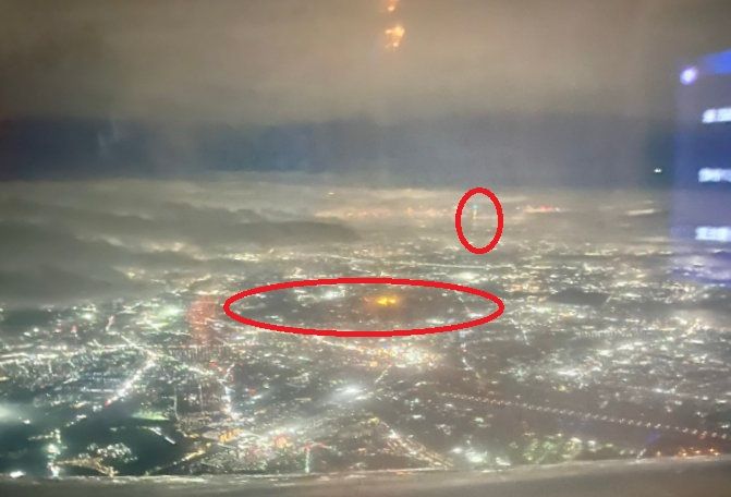 Picture of Tokyo from an airplane, with red circles superimposed to identify the Imperial Palace and the Tokyo SkyTree.  It's all kind of dark even if you don't have issues with eyes.  The blue rectangle to the right is obviously the entertainment monitor inside the airplane, reflecting on the window.  Looks like ANA, but I'm not sure.