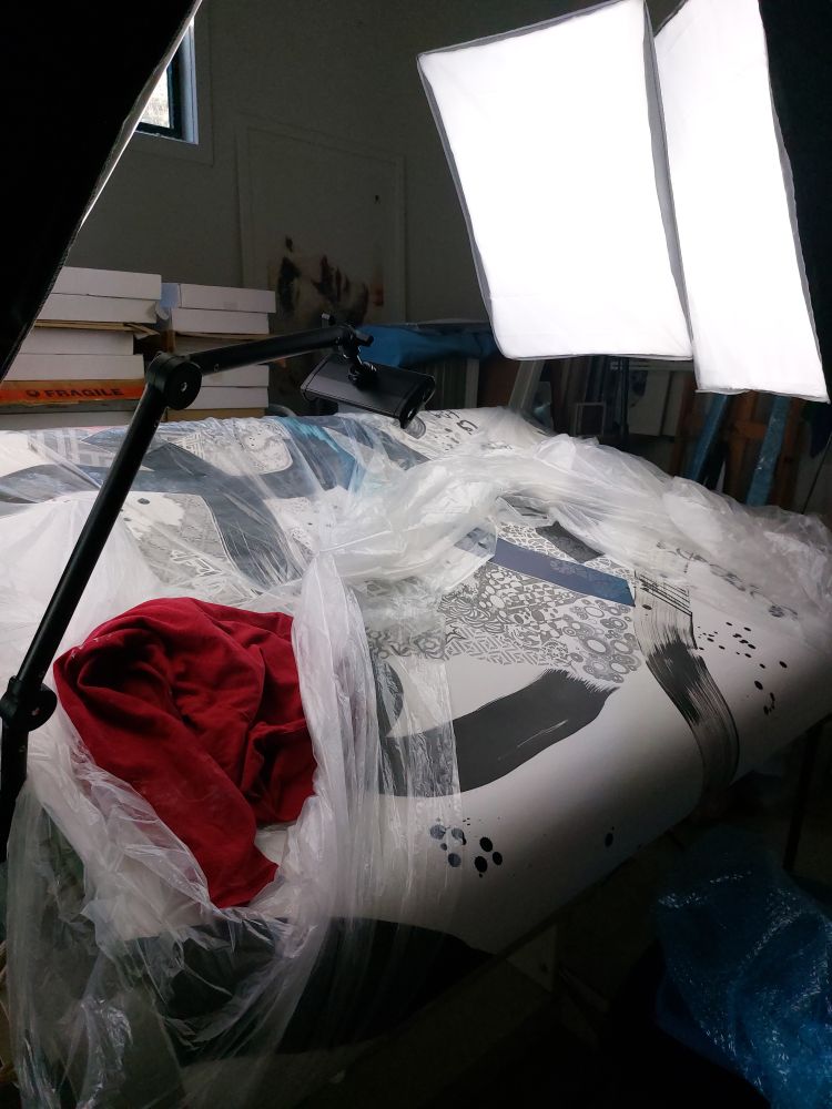 The drawing table used by Leith.  Three large photography lights with defusers shine upon the surface. Part, about 1 metre square, of an abstract and detailed drawing is visible.  A further 6 metres is rolled under the table surface.  The drawing is partially protected by plastic.