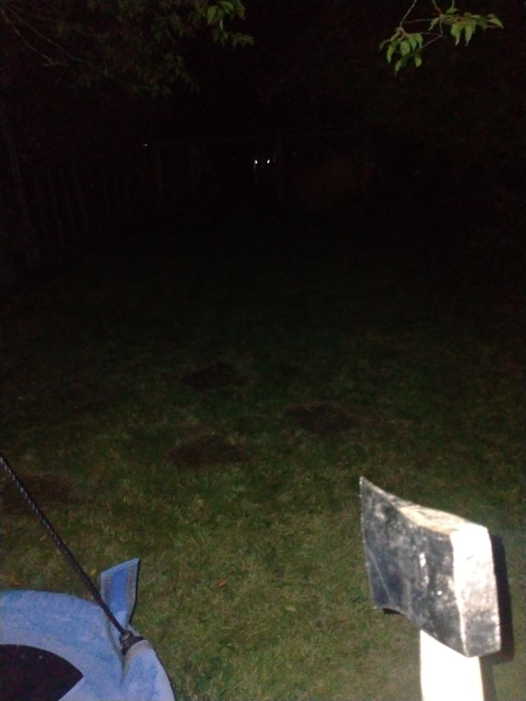 Photo at night with an axe being held next to a swing with two bright lights in the backdrop 