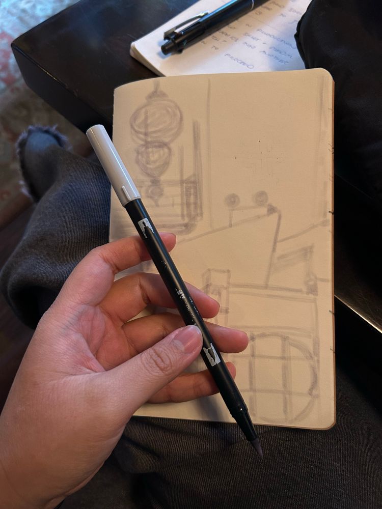 hand holding tombow n95 marker with a sketchbook underneath. there is the beginnings of a light sketch of a room interior 