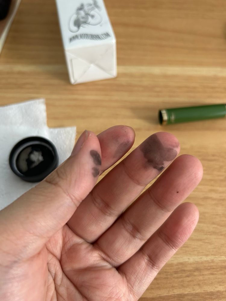hand with ink stained fingers. pen cap of green fountain pen and the cap of the open ink jar is on top of the desk behind the hand