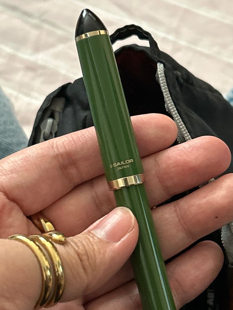 hand with gold rings holding a green sailor fountain pen
