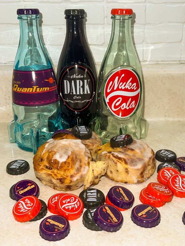 3 bottles specific to the fallout franchise stand tall behind 3 lazily places sweet rolls with nuka caps gracing their presence.
