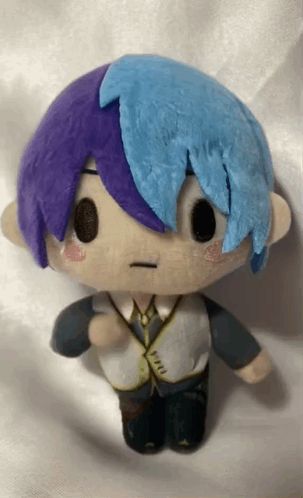 a stuffed toy with purple hair and blue hair is sitting on a white cloth