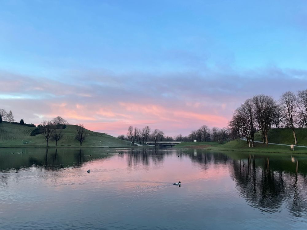 See und Hügel in rosa-blauem Sonnenaufgangslicht