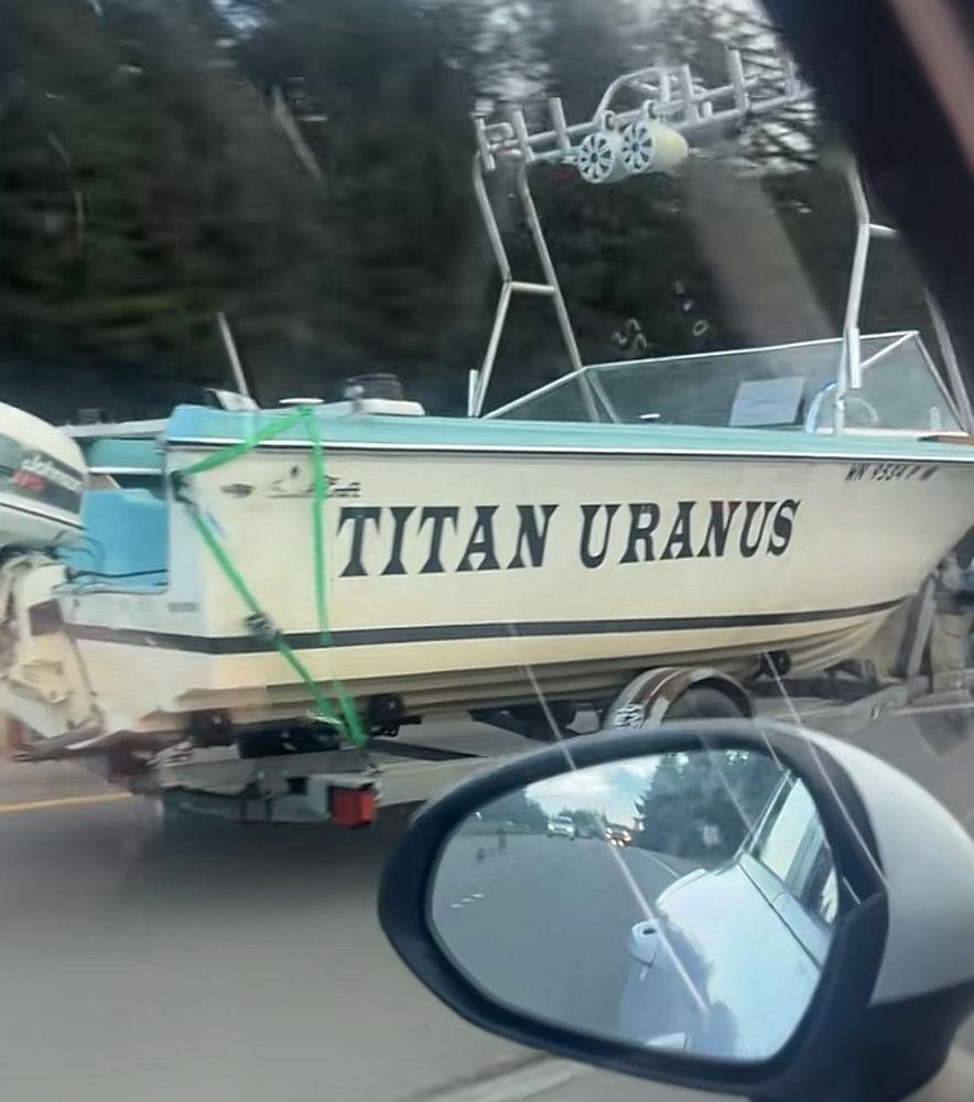A TikTok screenshot shows a person recording a towed boat from within their car. The boat is named Titan Uranus.