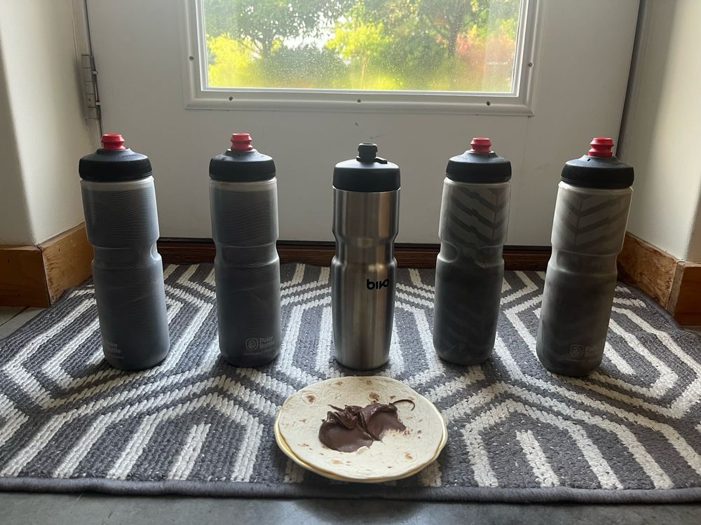 Five water bottles and a Nutella burrito in front of a window 