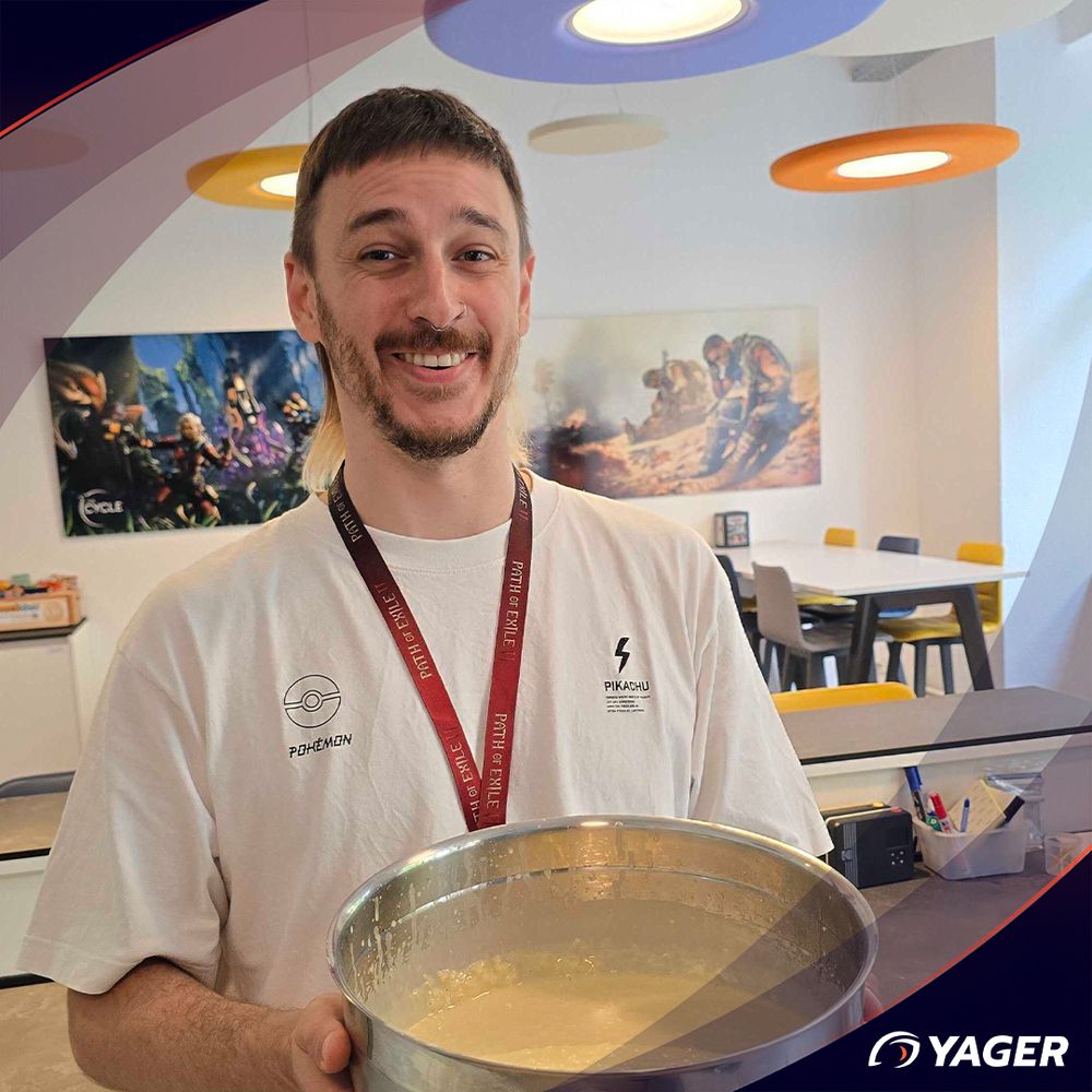 Male person holding a metal bowl full of waffle dough in an office kitchen in front of 2 game posters.