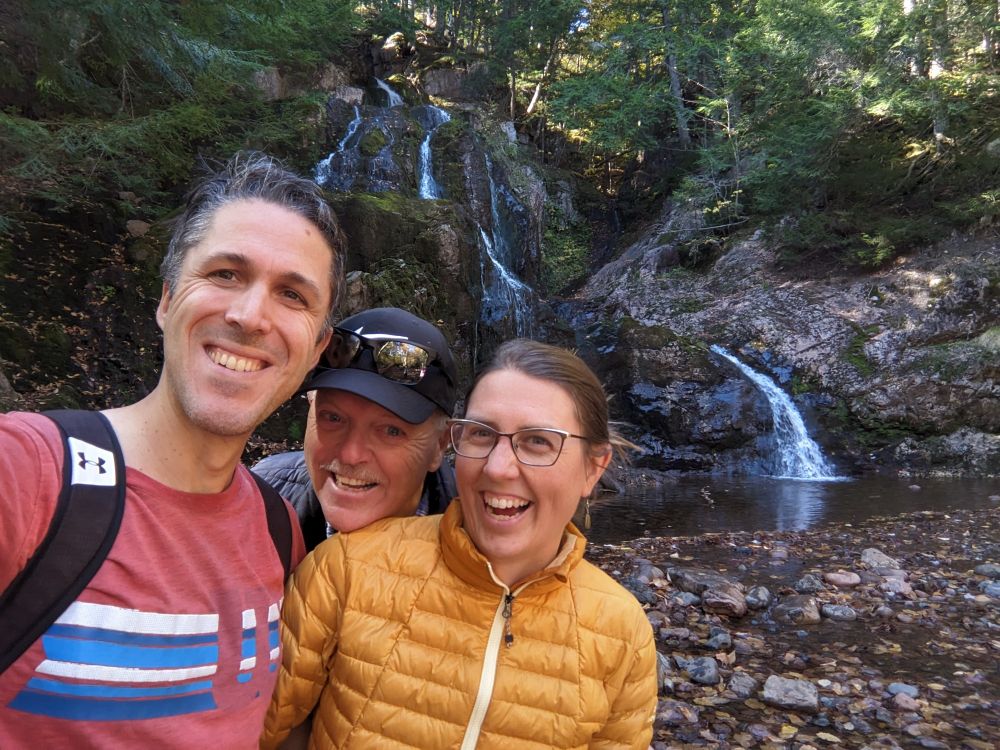 Three people laughing in front of a waterfall. 
