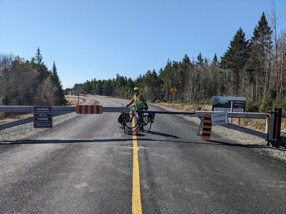 A cyclist on the other side of a gate saying CLOSED. The road is wide and there are trees on both sides. 