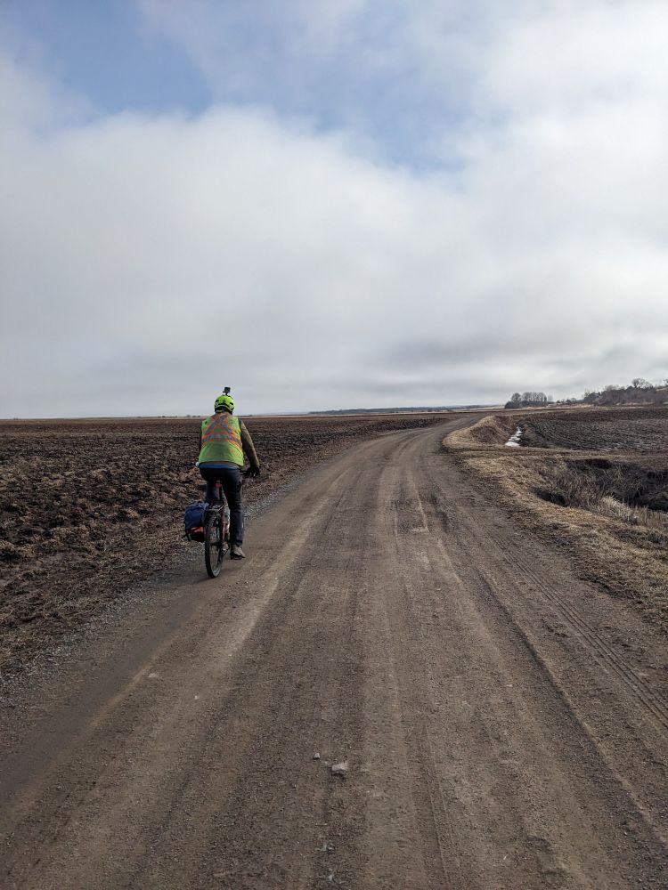 Cyclist in a yellow vest biking on a dirt road.