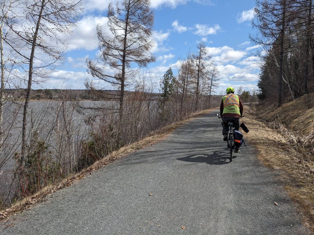 A cyclist riding along a gravel path next to a wide river. If you look closely you can see whitecaps indicating that it was windy!