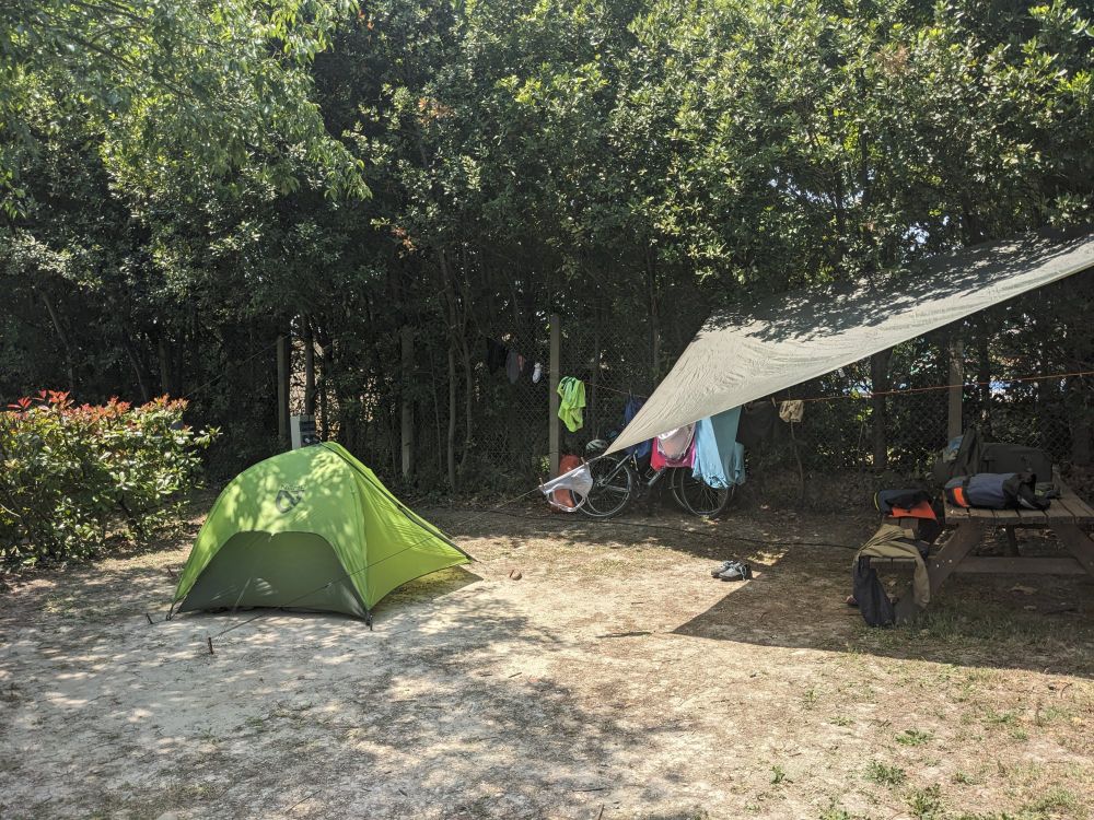 A small green tent is on the left and a picnic table covered in a tarp is on the right. 