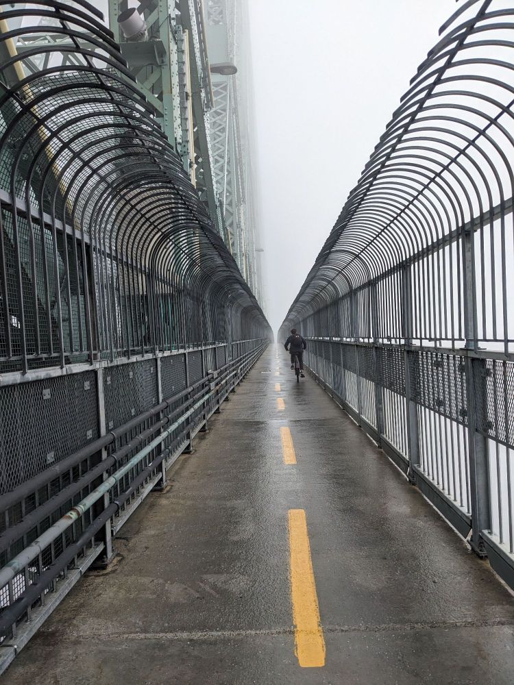 A cyclist riding across a bridge on a bike lane on a foggy day.