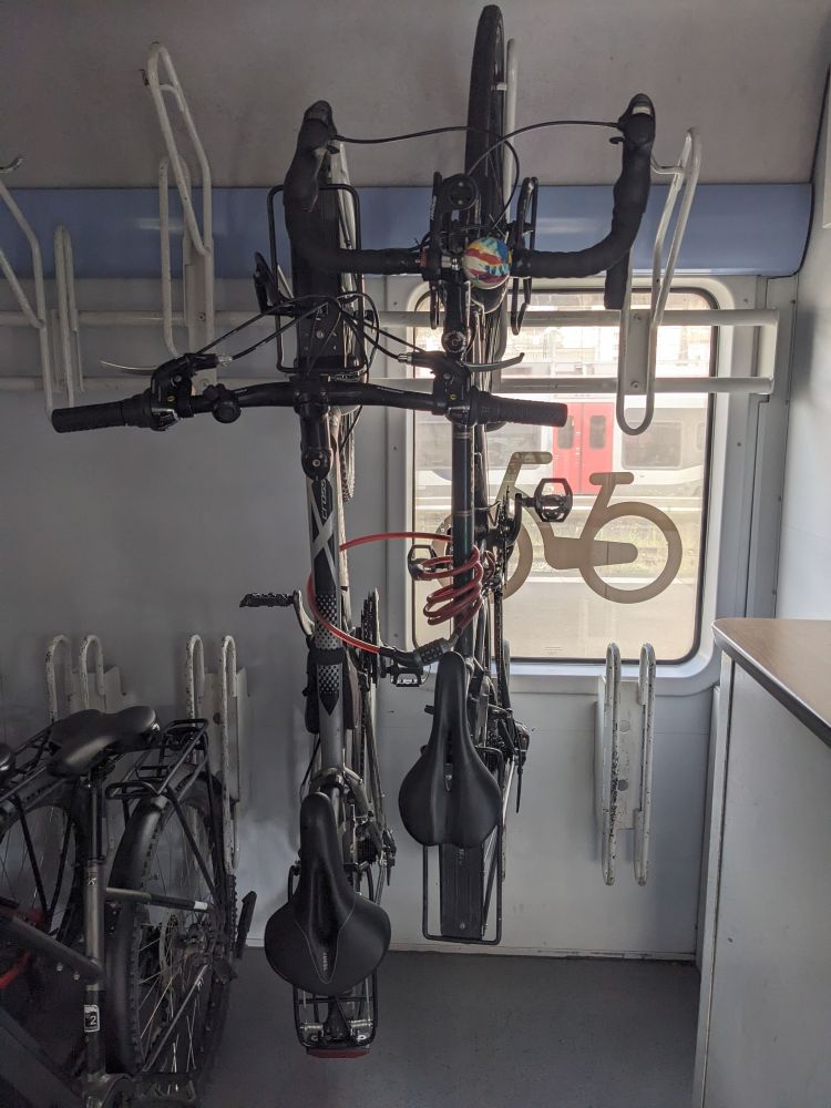 Two bikes handing on a train. There is another bike on the left that is not hanging. 